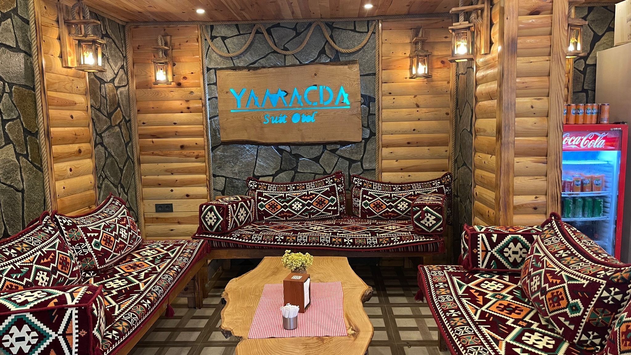 A log cabin-style room with a stone wall, wooden furniture, and a sign reading "YAMACDA Suite Room".