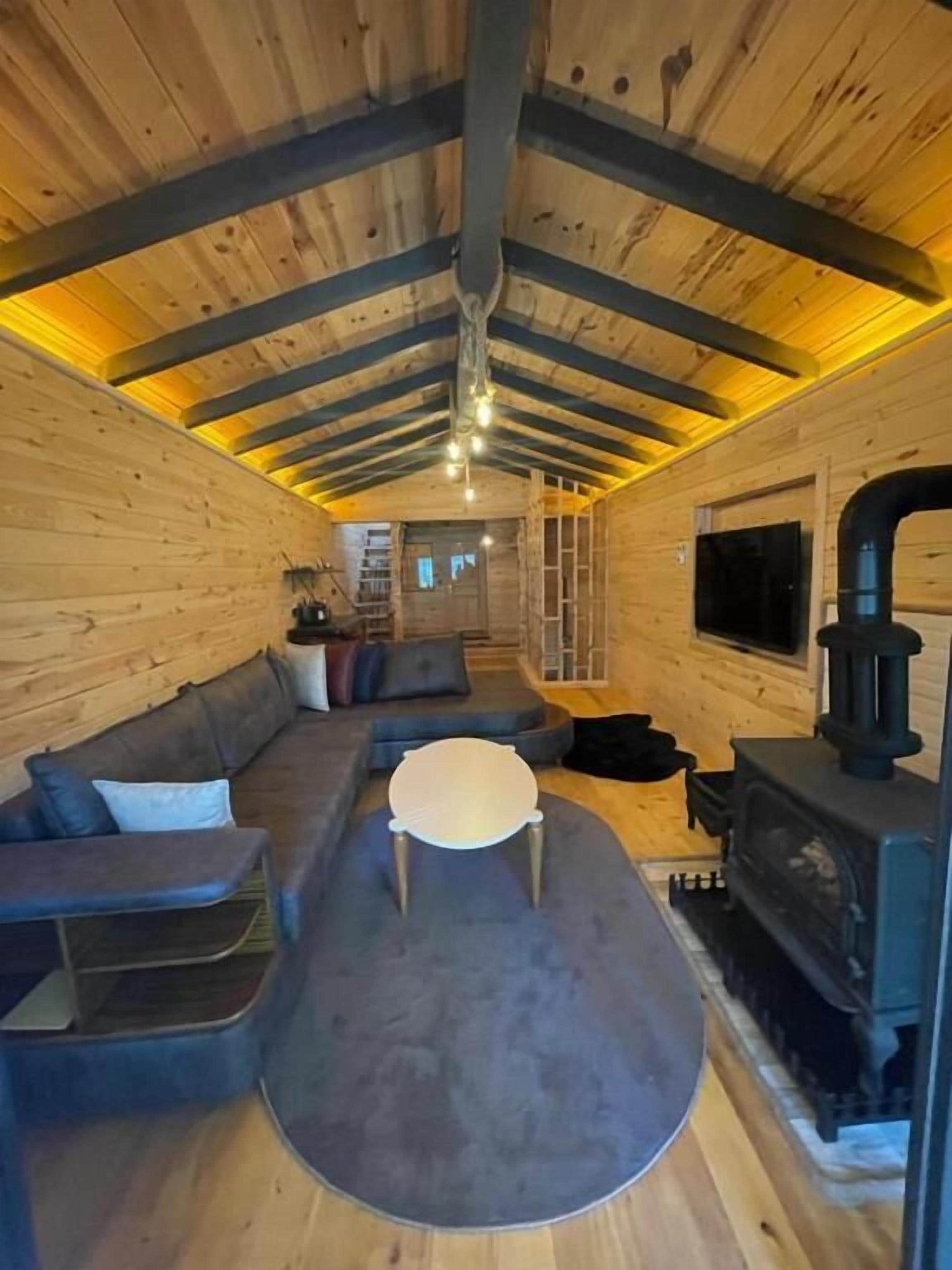 L’intérieur chaleureux d’un chalet, avec un revêtement mural en bois, un canapé, une table ronde et une cheminée.