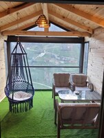 Un cuarto acogedor con un sillón colgante, dos sillones mullidos, una mesa de vidrio y vistas a un paisaje verde a través de un ventanal grande.