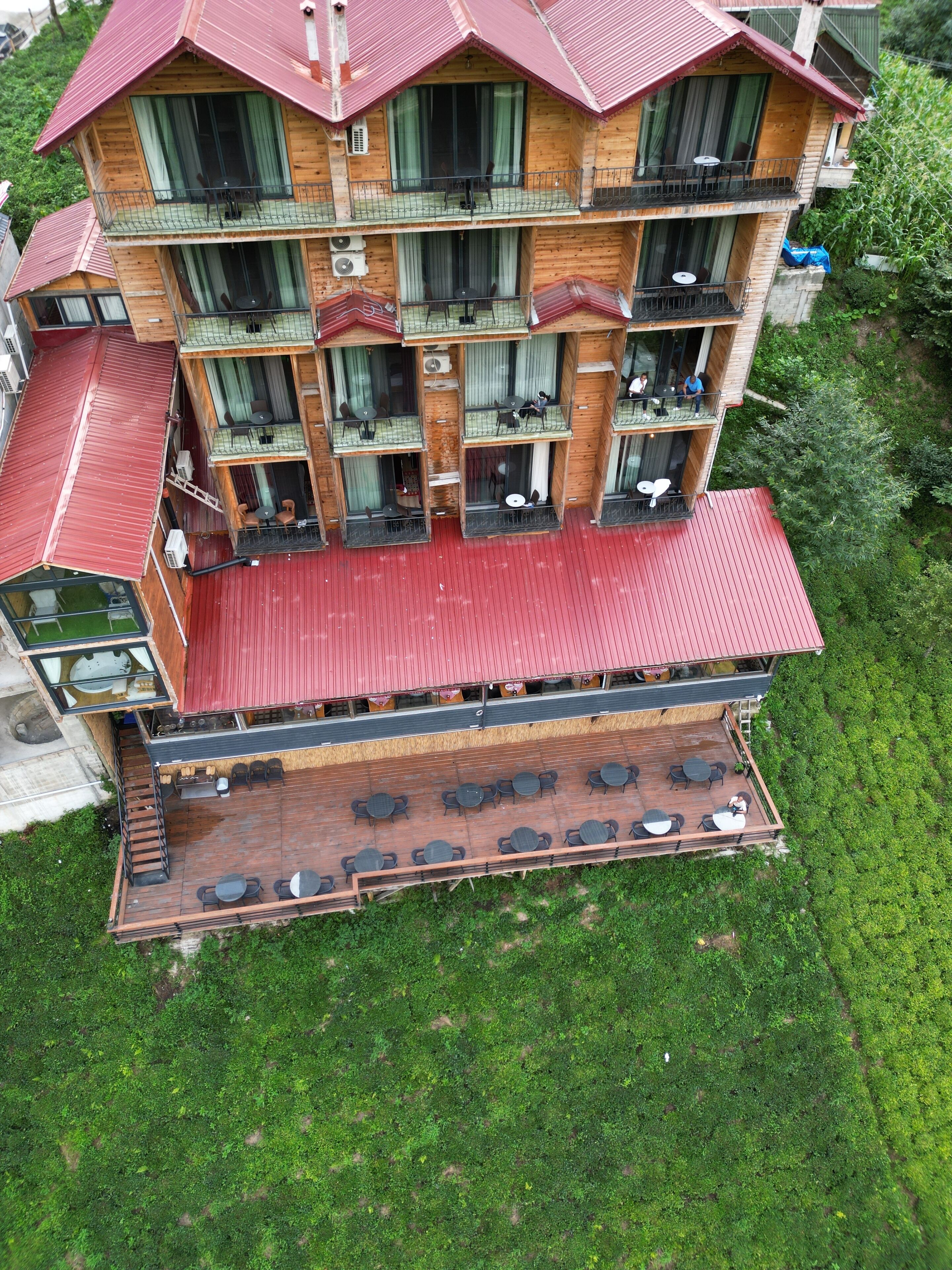 Un edificio de madera de varios pisos con balcones, mobiliario exterior y un techo rojo.