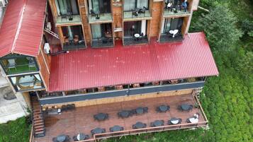 Un edificio de madera de varios pisos con balcones, mobiliario exterior y un techo rojo.