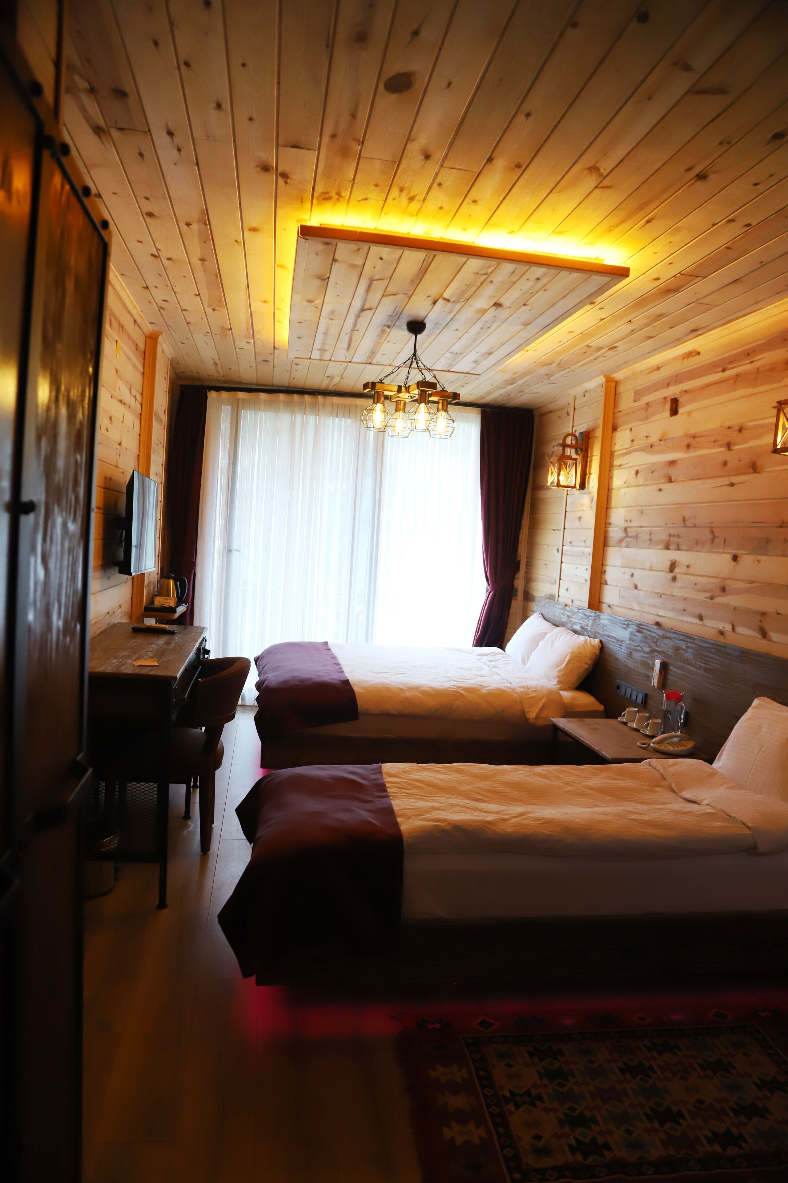 Een houten kamer in chaletstijl met twee bedden, een bureau en een televisie.