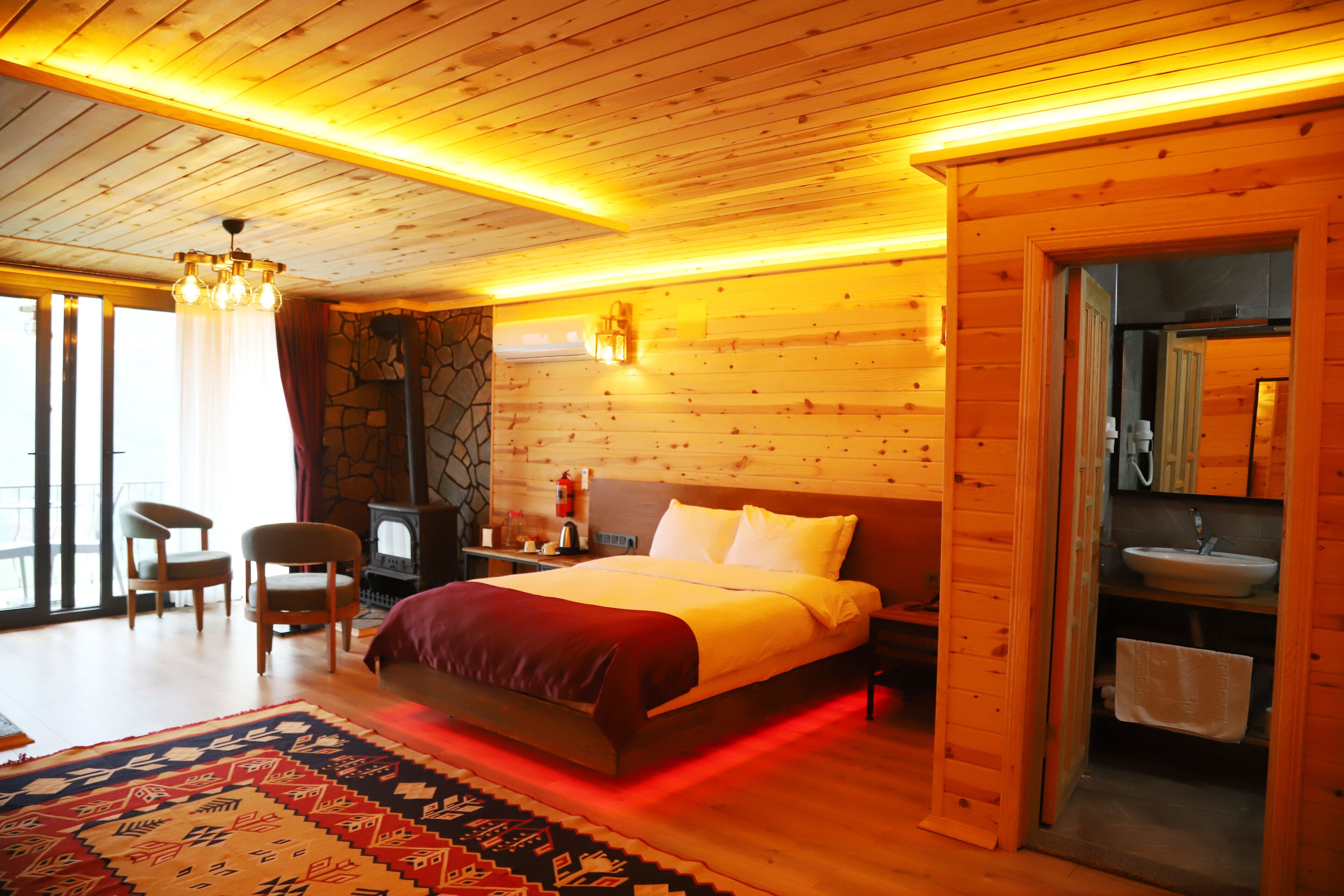 Een slaapkamer in een houten chalet, met een bed, twee stoelen, een vloerkleed en een stenen muur.