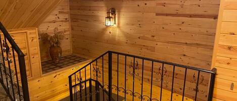 A wooden interior with a staircase, a wall-mounted light fixture, and a decorative vase.