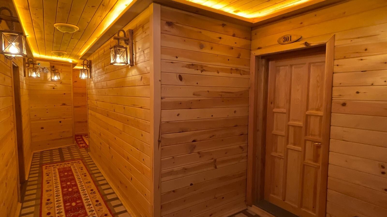 A wooden hallway with a patterned rug, wooden walls, and a door with a number plate.