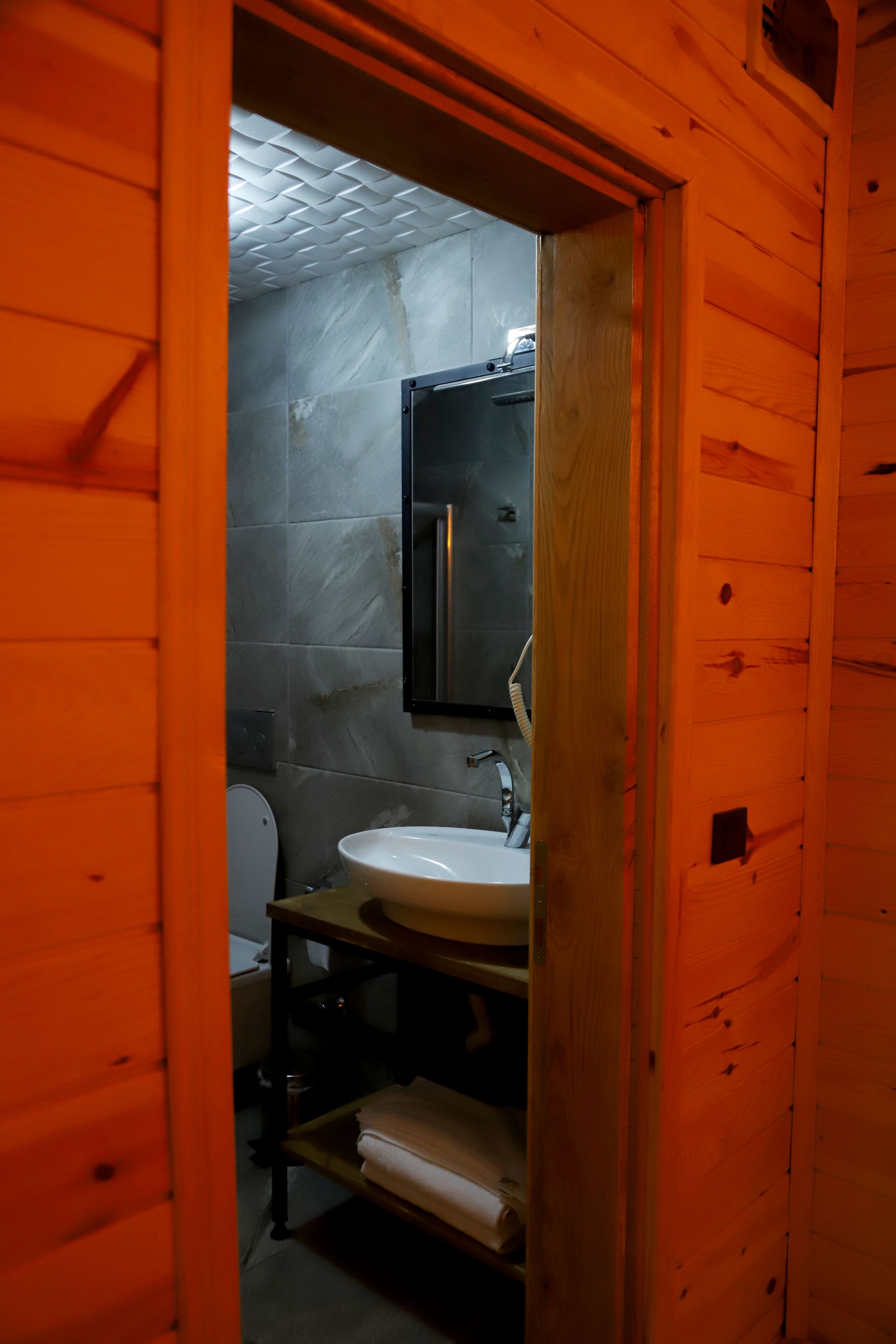A wooden-paneled bathroom with a white sink, a mirror, and a toilet.