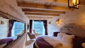 A wooden cabin-style bedroom with a large bed, a chair, and a view of the outdoors. - Yamaçda Suit Otel (Camlihemsin)