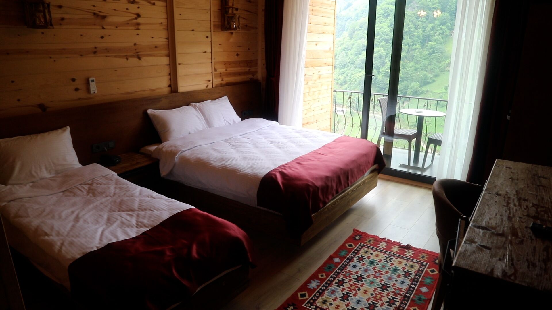 Una habitación con dos camas, piso de madera, alfombra estampada y balcón con mesa y sillas.