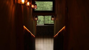 A dimly lit hallway with a window at the end, leading to a room with a stone wall and a bed. - Yamaçda Suit Otel (Camlihemsin)