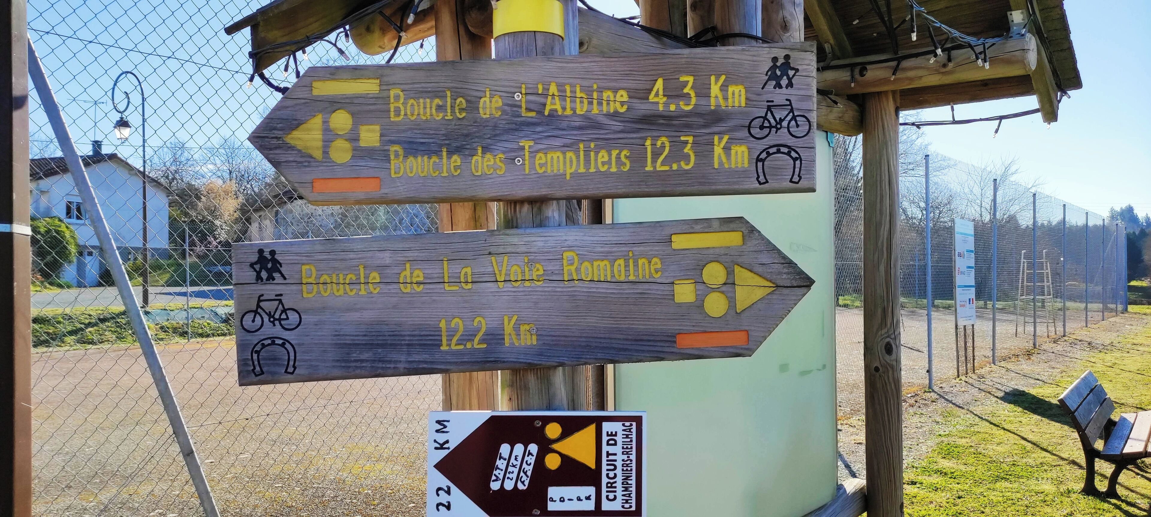 A wooden signpost with directional arrows and distances to various cycling routes.