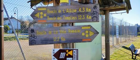 A wooden signpost with directional arrows and distances to various cycling routes.