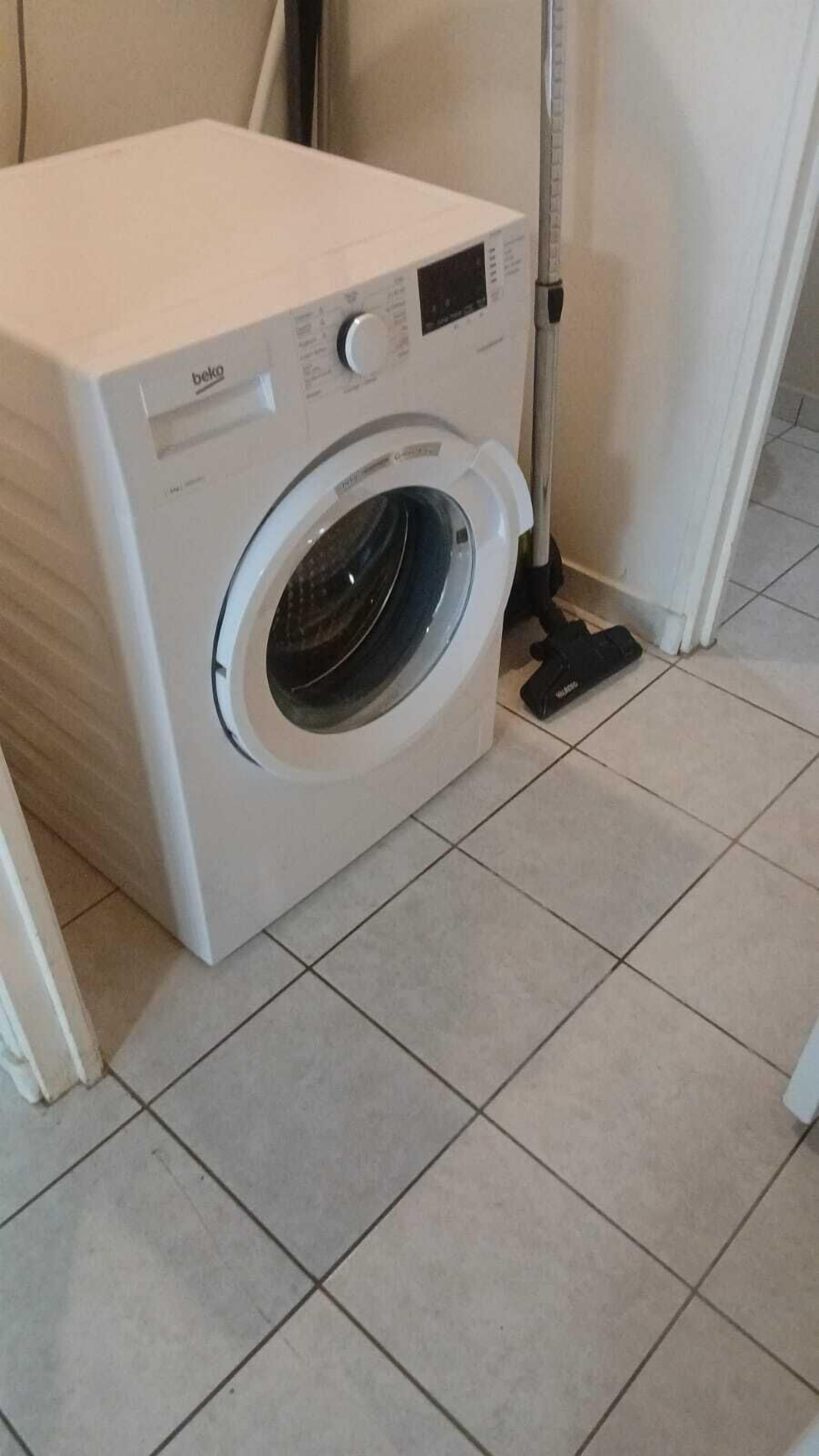 A front-loading washing machine in a room with tiled flooring.