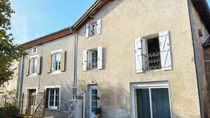 Ein zweistöckiges Gebäude mit weißen Fensterläden, einer steinernen Fassade und einem Ziegeldach.