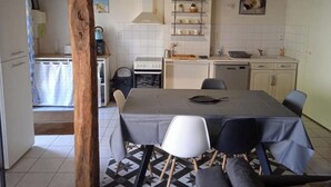 Eine kleine Küche mit weißen Schränken, einem Herd und einem Spülbecken. Es gibt einen Esstisch mit Stühlen und einem gemusterten Boden.
