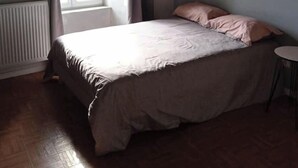 Ein Schlafzimmer mit Bett, einem Fenster mit Vorhängen, einem Heizkörper und einem kleinen Tisch.