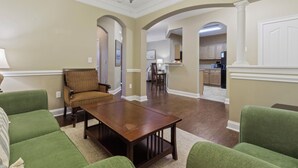 Amplia sala de estar con una mesa de centro de madera, sofás verdes y una zona de comedor con candelabro.