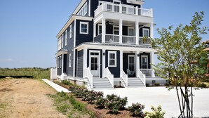 A two-story house with a balcony, a front porch, and a sandy driveway. - Bayfront Home Featuring Private Beach Access in Bay Creek! (Cape Charles)