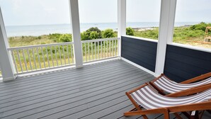 A covered porch with a view of the ocean, wooden chairs, and a railing. - Bayfront Home Featuring Private Beach Access in Bay Creek! (Cape Charles)