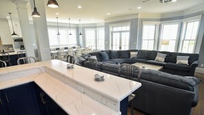 A modern kitchen with a marble countertop, dark cabinets, and a large L-shaped gray sectional sofa. - Bayfront Home Featuring Private Beach Access in Bay Creek! (Cape Charles)
