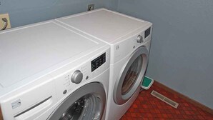 A compact, white, front-loading washing machine in a small laundry room with a tiled floor and a blue wall. - 584 Alpine Drive in South Lake Tahoe, CA (South Lake Tahoe)