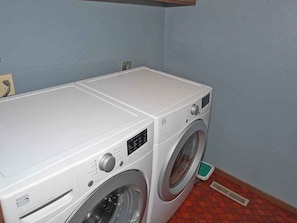 Una lavadora blanca y compacta de carga frontal en un pequeño cuarto de lavado con piso de baldosas y pared azul.