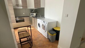 Une cuisine compacte équipée d’un lave-linge, d’un four à micro-ondes et d’un petit coin repas avec un banc.