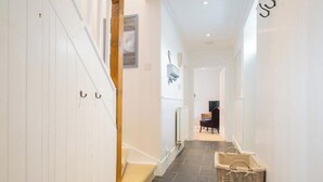 A narrow hallway with white walls, a wooden staircase, a black chair, and a wicker basket. - Pretty cottage on Moray coast: walks & whisky (Buckie)