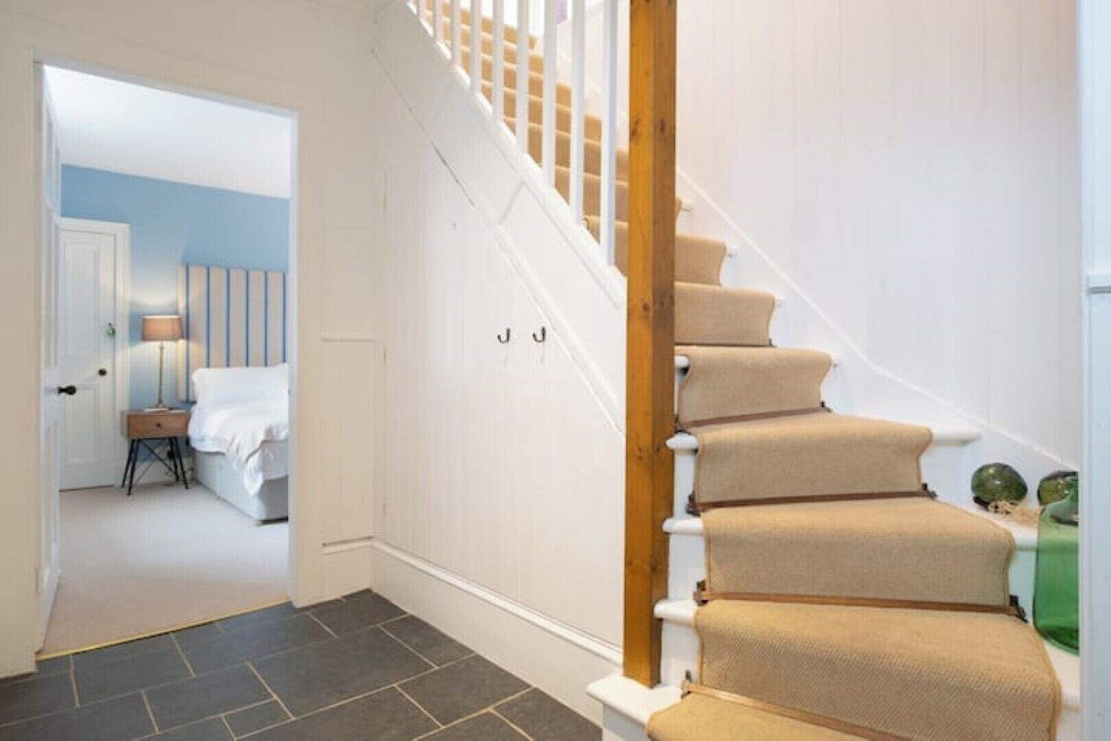 Una escalera con alfombra color beige y barandillas blancas que conduce a un dormitorio con cama y mesita de noche.