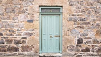 Un edificio de piedra con una puerta azul claro, una placa con un número encima de la puerta y un letrero en la pared que dice "SEASPRAY".
