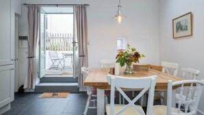 A dining area with a wooden table, white chairs, a hanging light fixture, and a vase with flowers. - Pretty cottage on Moray coast: walks & whisky (Buckie)
