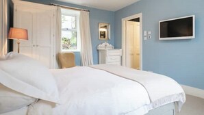 A bedroom with a large bed, a chair, a dresser, and a television on the wall. - Pretty cottage on Moray coast: walks & whisky (Buckie)