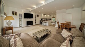 A modern living room with a sofa, coffee table, and a TV. There is a kitchen in the background with a dining area. -  Serviced Apartments Macclesfield (Macclesfield)