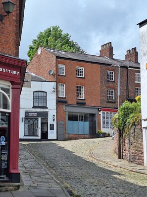 A cobblestone street with buildings, including a barbers' lounge and a building with a red sign. -  Serviced Apartments Macclesfield (Macclesfield)