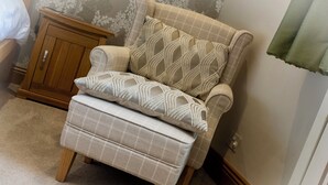 A corner armchair with a matching ottoman, a wooden cabinet, and a patterned wall. -  Serviced Apartments Macclesfield (Macclesfield)