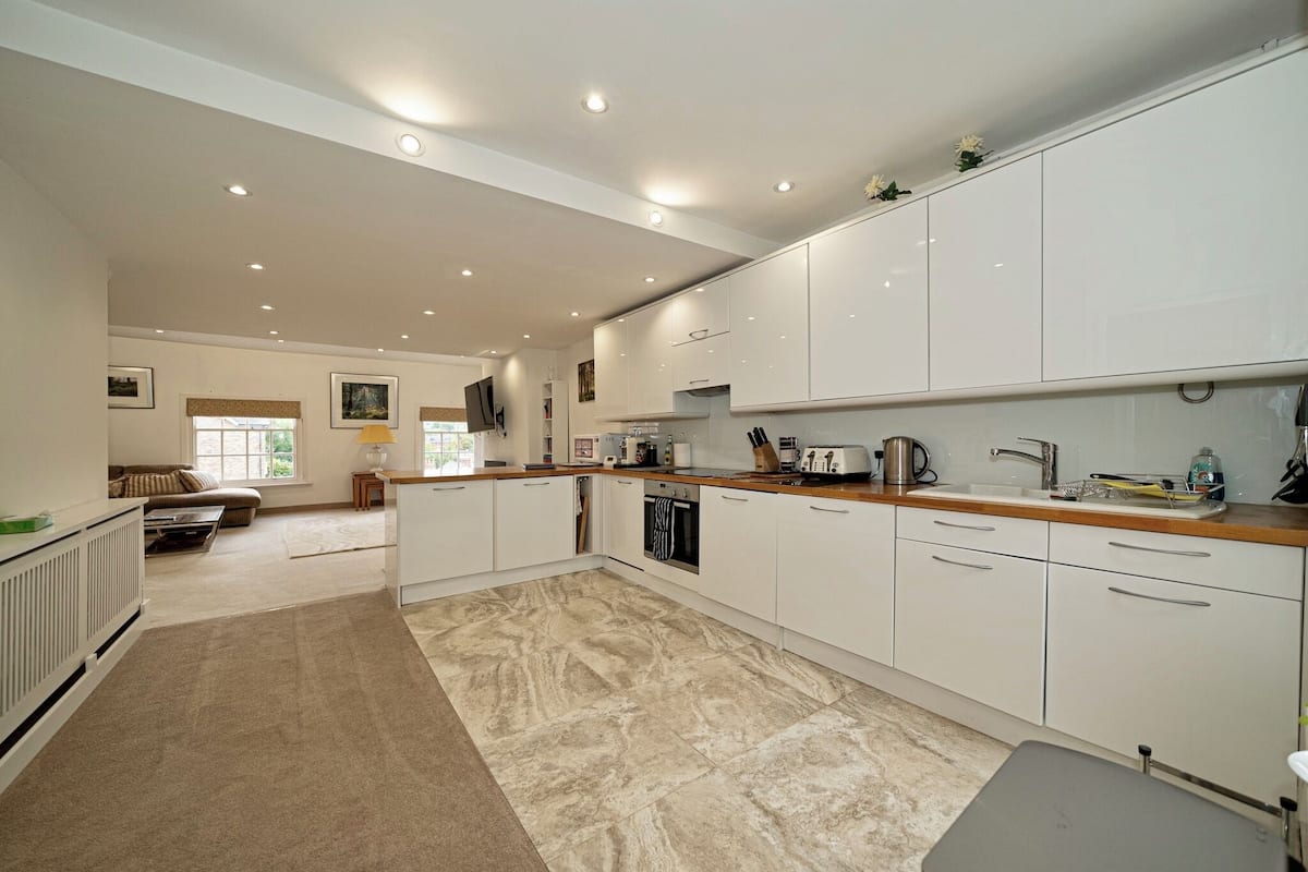 A spacious kitchen with white cabinets, a wooden countertop, and a tiled floor.