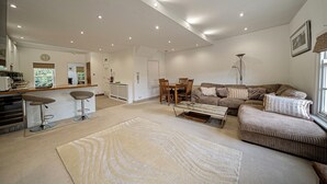 A spacious living room with a large sectional sofa, a dining area with a wooden table and chairs, and a kitchen area with bar stools. -  Serviced Apartments Macclesfield (Macclesfield)