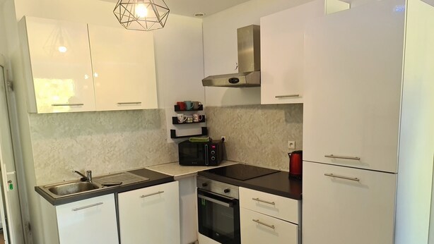 A modern kitchen with white cabinets, a stainless steel sink, a microwave, a kettle, and a built-in oven.