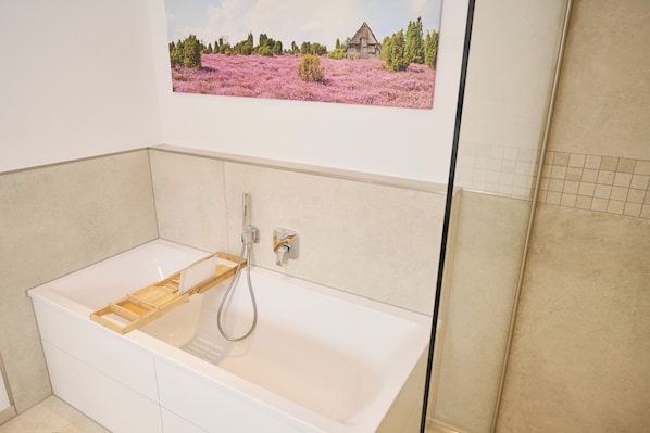 A bathroom with a bathtub, a wooden shelf, and a shower.