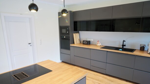 Een moderne keuken met grijze kastjes, een houten aanrechtblad en een zwarte afzuigkap.