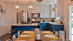 A modern kitchen with white cabinets, a blue island, stainless steel appliances, and a dining area with yellow placemats and white plates.
