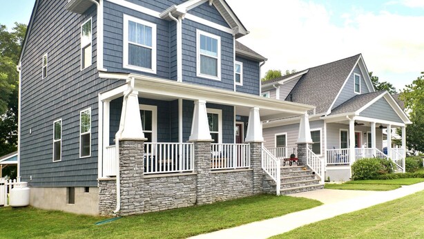 A two-story house with a stone foundation, a front porch with white railings, and a grey roof.