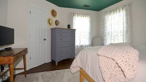A bedroom with a bed, a dresser, a television on a desk, and a door.