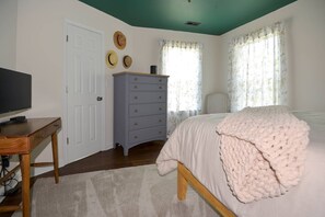 A bedroom with a bed, a dresser, a television on a desk, and a door. - Salty Sea Shack, Near Park, Beach & Pet-Friendly (Cape Charles)