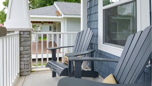 A porch with Adirondack chairs, a stone pillar, and a view of a house with a covered deck.