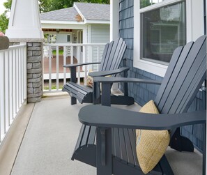 Een veranda met Adirondack-stoelen, een stenen pilaar en uitzicht op een huis met een overdekt terras.