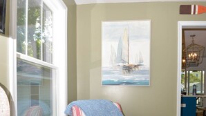 A striped armchair with a pillow, a painting of sailboats, and a wooden floor.