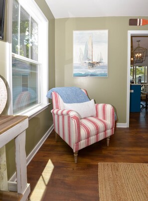 Un sillón a rayas con un cojín, un cuadro de veleros y un suelo de madera.