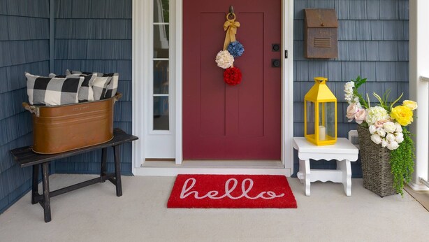 A red door with a 'hello' mat, a mailbox, and a sign reading 'The Salty Sea Shack' above the door.