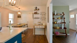 A kitchen with a central island, wooden shelves, and a dining area with chairs and a table.