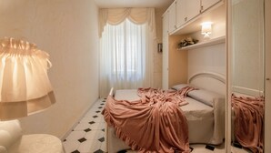 Un dormitorio con cama, mesita de noche, espejo y ventana con cortinas.